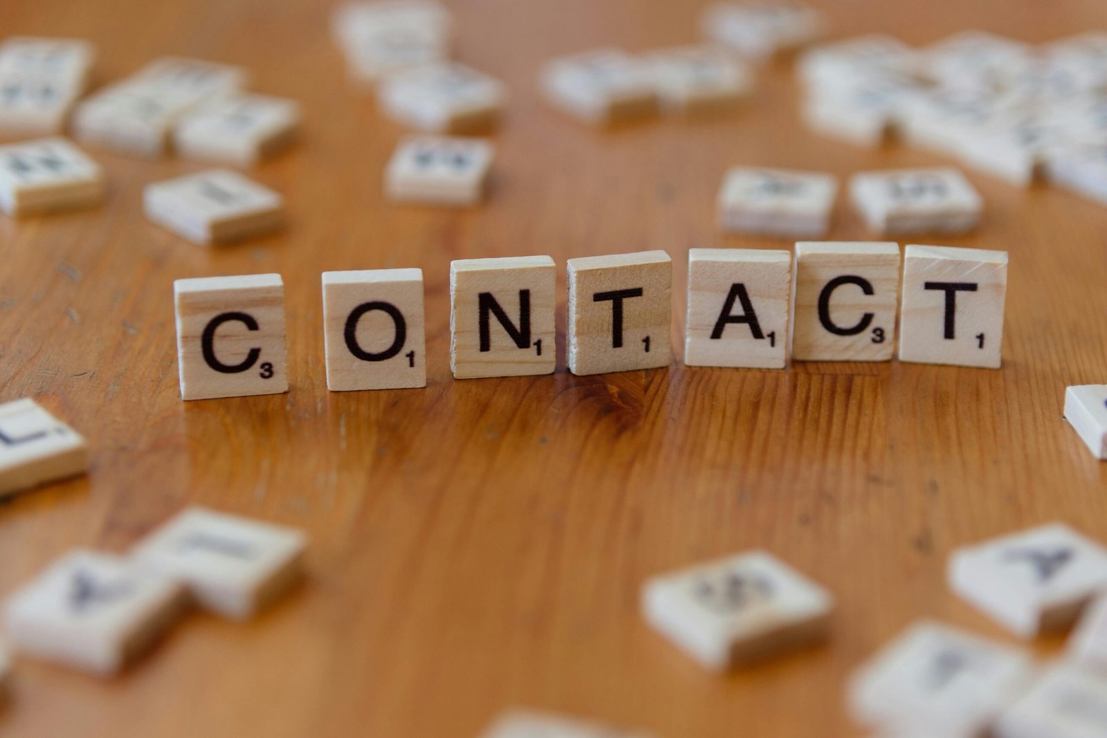 Scrabble letters spelling 'contact' on a wooden table surface.